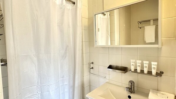 Ein Badezimmer mit Duschvorhang, Spiegel, Waschbecken und Pflegeprodukten auf einem Regal.