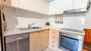 A compact kitchen with a dishwasher, sink, wooden cabinets, and a built-in oven.