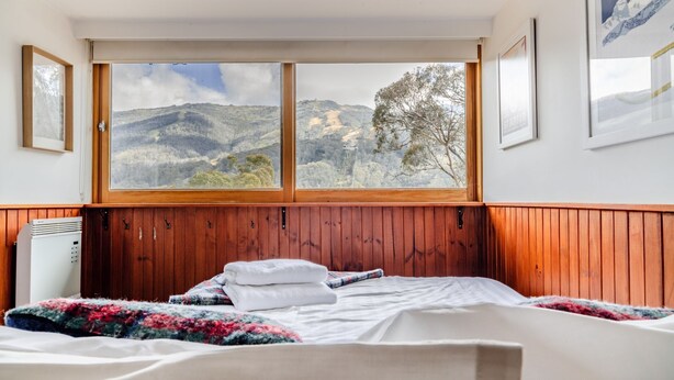 A bedroom with a wooden headboard, a bed with white linens, a window with a mountain view, and a heater on the wall.