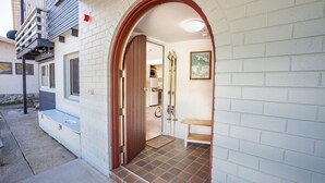 A white brick building with a wooden archway entrance, a small wooden bench, and a tiled floor.