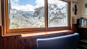 A room with a large window overlooking a mountainous landscape, a wooden bench, and a bookshelf with books.