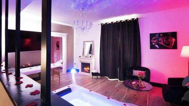 A modern room with a fireplace, a chandelier, a sofa, and a table with a vase of flowers. - Dream Room | Jacuzzi, Sauna, Waterbed (Forbach)