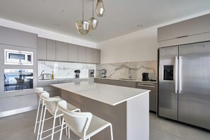 A modern kitchen with a large island, bar stools, stainless steel appliances, and a marble backsplash.