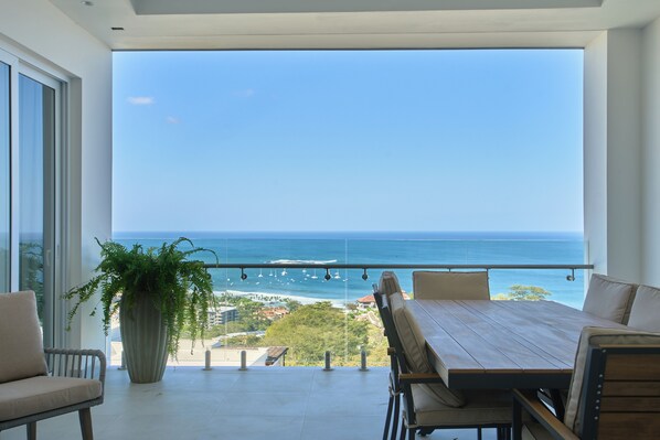 A balcony with a view of the ocean, a potted plant, and a wooden table with chairs.