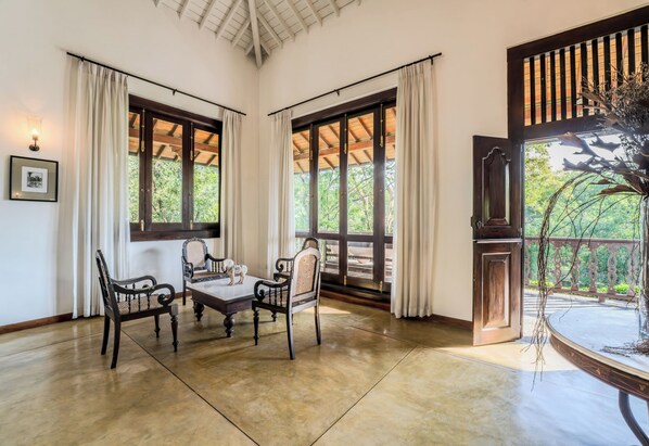 Una habitación con una mesa y sillas de madera, ventanas amplias con cortinas, y vistas a zonas verdes.