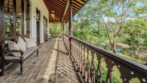 Un espacio al aire libre cubierto con un banco de madera y barandilla, con vistas a un jardín y una masa de agua.