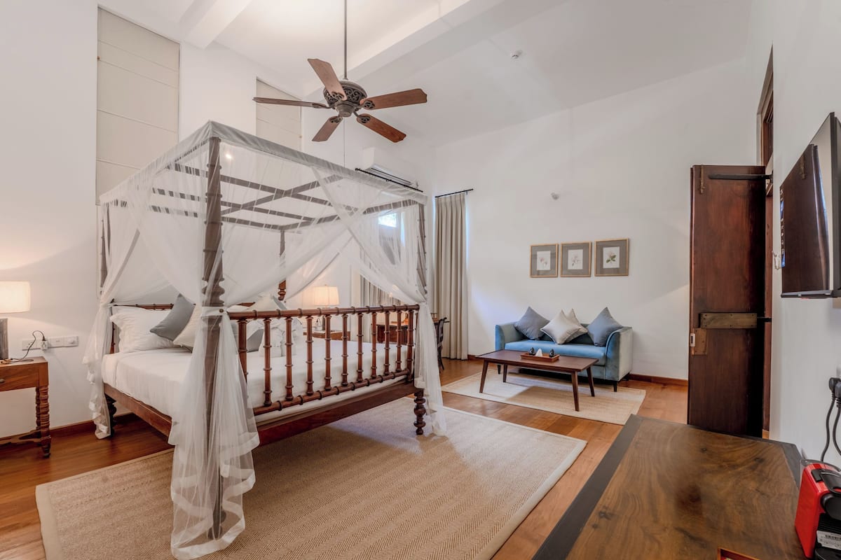 A bedroom with a four-poster bed, a ceiling fan, a sofa, a coffee table, and a TV.