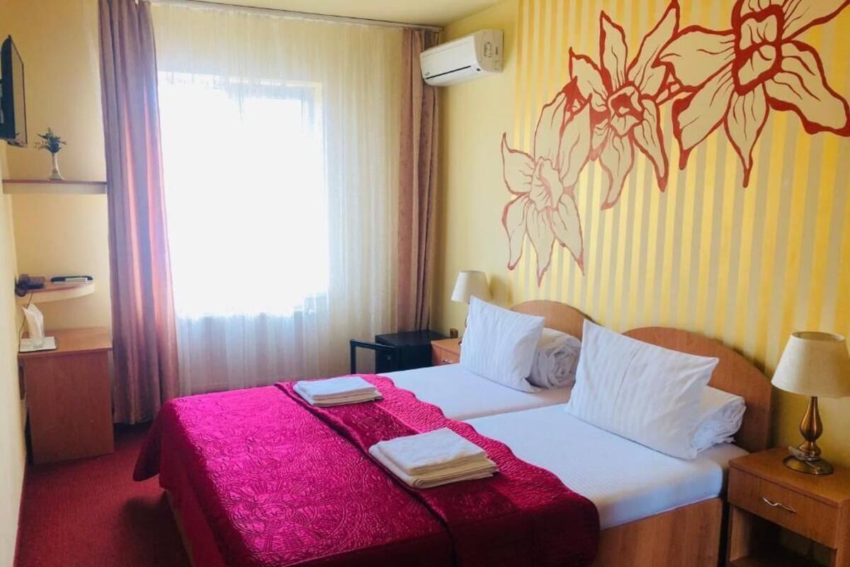 Une chambre d’hôtel avec un grand lit, deux oreillers, une couvre-lit rouge, une lampe de chevet, une table de chevet et un climatiseur fixé au mur.
