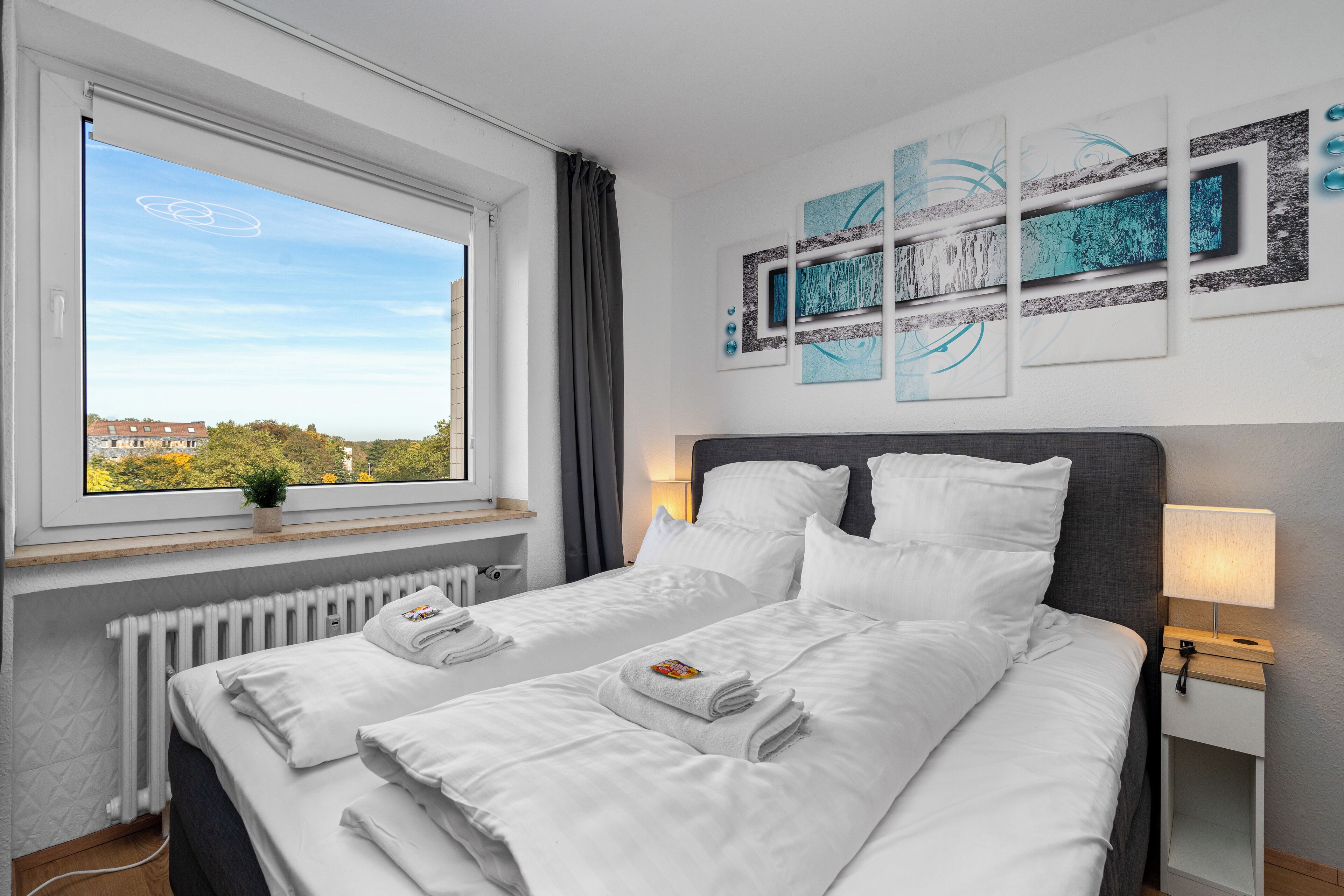 Une chambre d’hôtel avec deux lits, une fenêtre donnant sur des immeubles, un radiateur et des œuvres d’art murales.