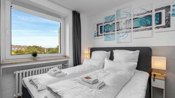 Une chambre d’hôtel avec deux lits, une fenêtre donnant sur des immeubles, un radiateur et des œuvres d’art murales.
