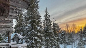 A log cabin with a snow-covered deck and a view of snow-covered trees.