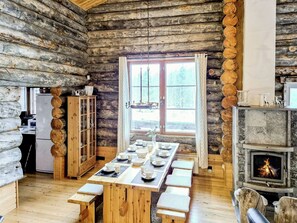 A log cabin interior with a dining table set for four, a fireplace, and a kitchen area. - Villa rokova by Interhome (Kuusamo)