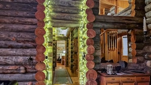 A log cabin interior with a central wooden archway adorned with lights, wooden walls, and a visible staircase.