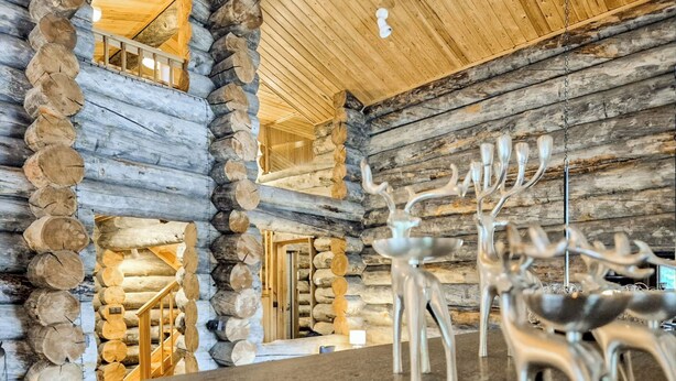 A log cabin interior with a central dining area, wooden walls, and a high ceiling.