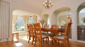 A dining room with wooden chairs and a table, large windows with curtains, and a chandelier. - 4 Bed House-sleeps 8-parking-pets-marinaseaview (Torquay)