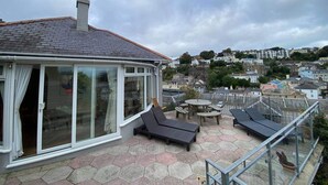 A covered outdoor area with a glass door, a small table, and lounge chairs. - 4 Bed House-sleeps 8-parking-pets-marinaseaview (Torquay)