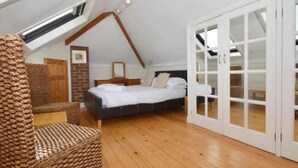 A bedroom with a sloped ceiling, wooden flooring, a bed, a chair, and a wardrobe with glass doors. - 4 Bed House-sleeps 8-parking-pets-marinaseaview (Torquay)