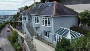 A two-story house with a sloped roof, large windows, and a visible staircase leading to the upper floor. - 4 Bed House-sleeps 8-parking-pets-marinaseaview (Torquay)