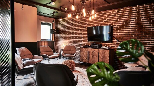 Un espace de détente moderne avec des fauteuils en cuir, un téléviseur et un mur en briques.