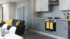 Une cuisine moderne avec des meubles gris, une hotte en acier inoxydable et un coin repas agrémenté d’un canapé noir et de coussins jaunes.