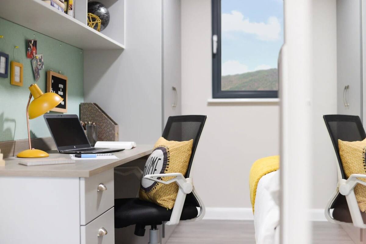 A modern office space with a desk, laptop, and two ergonomic chairs with yellow cushions.