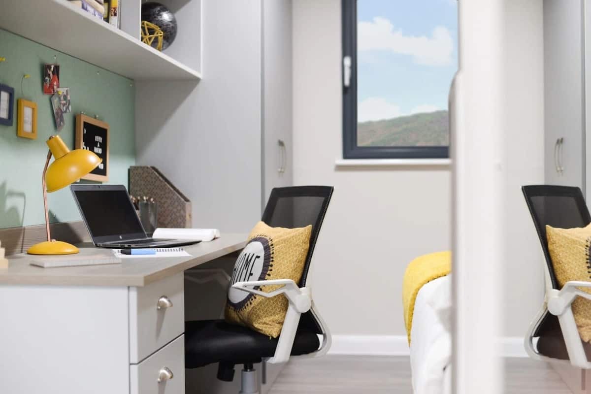 A modern office space with a desk, laptop, and two ergonomic chairs with yellow cushions.