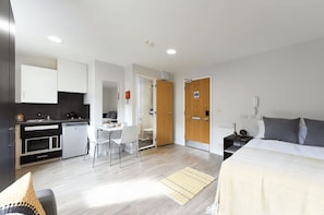 Une chambre d’hôtel moderne équipée d’un lit, d’un petit bureau, d’une kitchenette et d’une salle de bain.