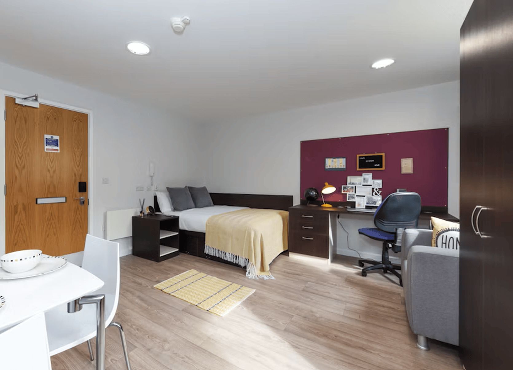 A modern bedroom with a bed, desk, chair, and a small table with cups.