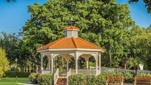 A gazebo with a tiled roof, surrounded by a well-maintained lawn and trees.