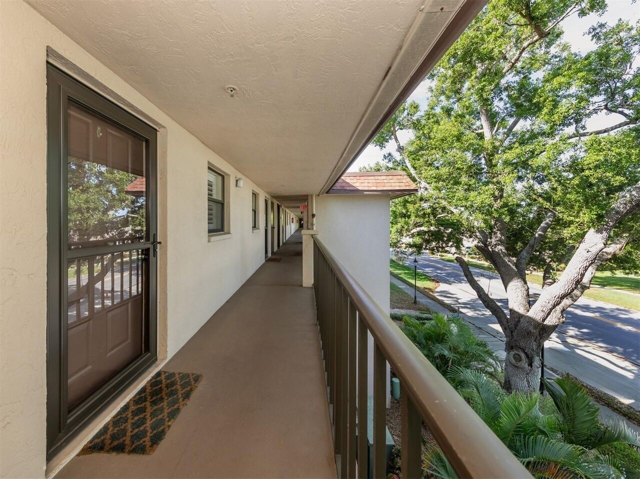 A covered corridor with a door, windows, and a view of a tree and street.