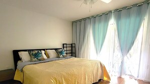 A bedroom with a bed, a ceiling fan, and curtains.