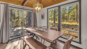 Spiseområde med et træbord, bænke og store vinduer med udsigt over en skov.