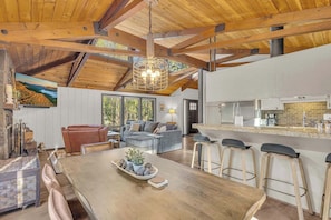 A spacious living area with a wooden ceiling, a dining table with bar stools, a sofa, and a kitchen area with a countertop and bar stools. - Private hot tub, dog friendly, great location (Sunriver)