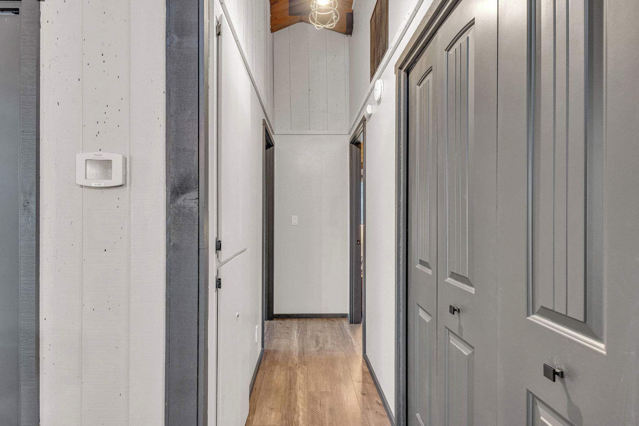 A narrow hallway with wooden flooring, white walls, and grey doors.