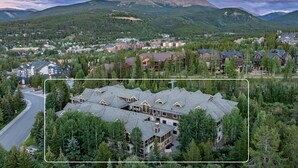 Un chalet doté d’un bâtiment principal entouré d’arbres, situé dans une région montagneuse, avec une ville en arrière-plan.