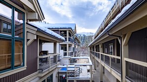 Un immeuble à plusieurs étages doté de balcons, d’un espace extérieur aménagé et couvert, et offrant une vue sur des montagnes enneigées.