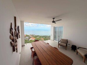 Un balcon avec vue sur l’océan, une table en bois et un ventilateur de plafond.