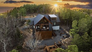A cabin with a deck and outdoor seating area, surrounded by trees and a forested landscape. - Luxury Forest Escape | NEW POOL, Loft, Swings Fire Pit &  gorgeous nature views (Broken Bow)