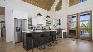 A modern kitchen with a central island, stainless steel appliances, and a large window overlooking a deck. - Luxury Forest Escape | NEW POOL, Loft, Swings Fire Pit &  gorgeous nature views (Broken Bow)