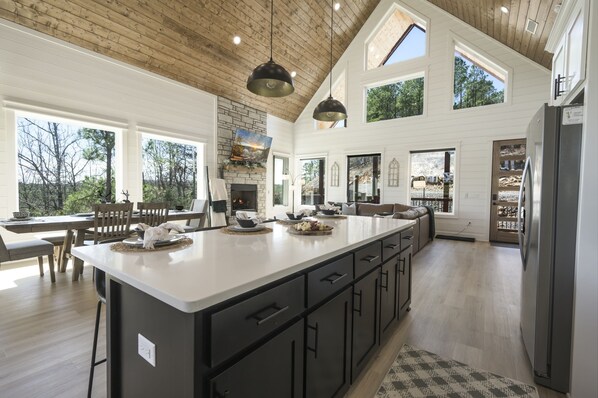 Enjoy cooking in this well-equipped kitchen with a large island, oven, and high ceiling with large windows offering views of the surrounding landscape.