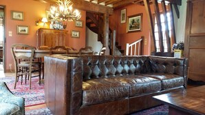 A cozy living room with a leather sofa, wooden dining table, and a chandelier. - La chasse - a beautiful cottage between coast and countryside (Anglesqueville-la-Bras-Long)