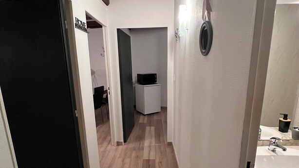 A narrow hallway with wooden flooring, a white sink, and a microwave in a small kitchenette area.