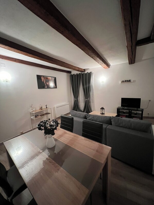 A modern living room with a wooden dining table, grey sofa, and a TV stand. - Spacious, fully-equipped accommodation  (Grandvillars)
