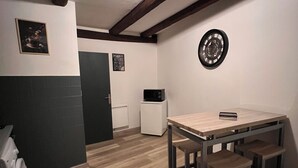 A compact kitchen with a wooden table and bench, a microwave, and a clock on the wall.