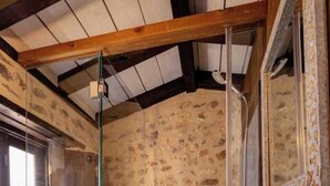 Une salle de bain avec un mur en pierre, une douche en verre, un lavabo blanc et une fenêtre.