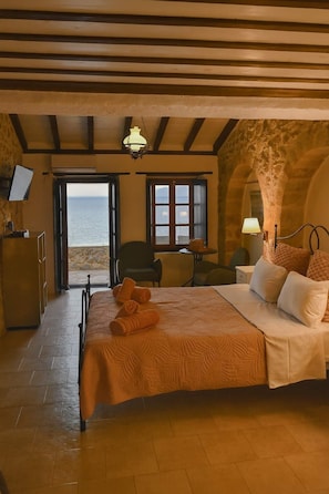 Quarto com cama, escrivaninha, cadeira e vista para o mar por uma porta.
