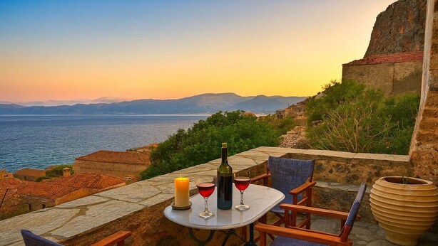 Ein Tisch mit Kerze, Weinflasche und Gläsern auf einer Steinterrasse mit Blick aufs Meer.
