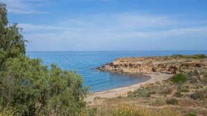 Eine Küstenlandschaft mit Strand, Felsen und spärlicher Vegetation.