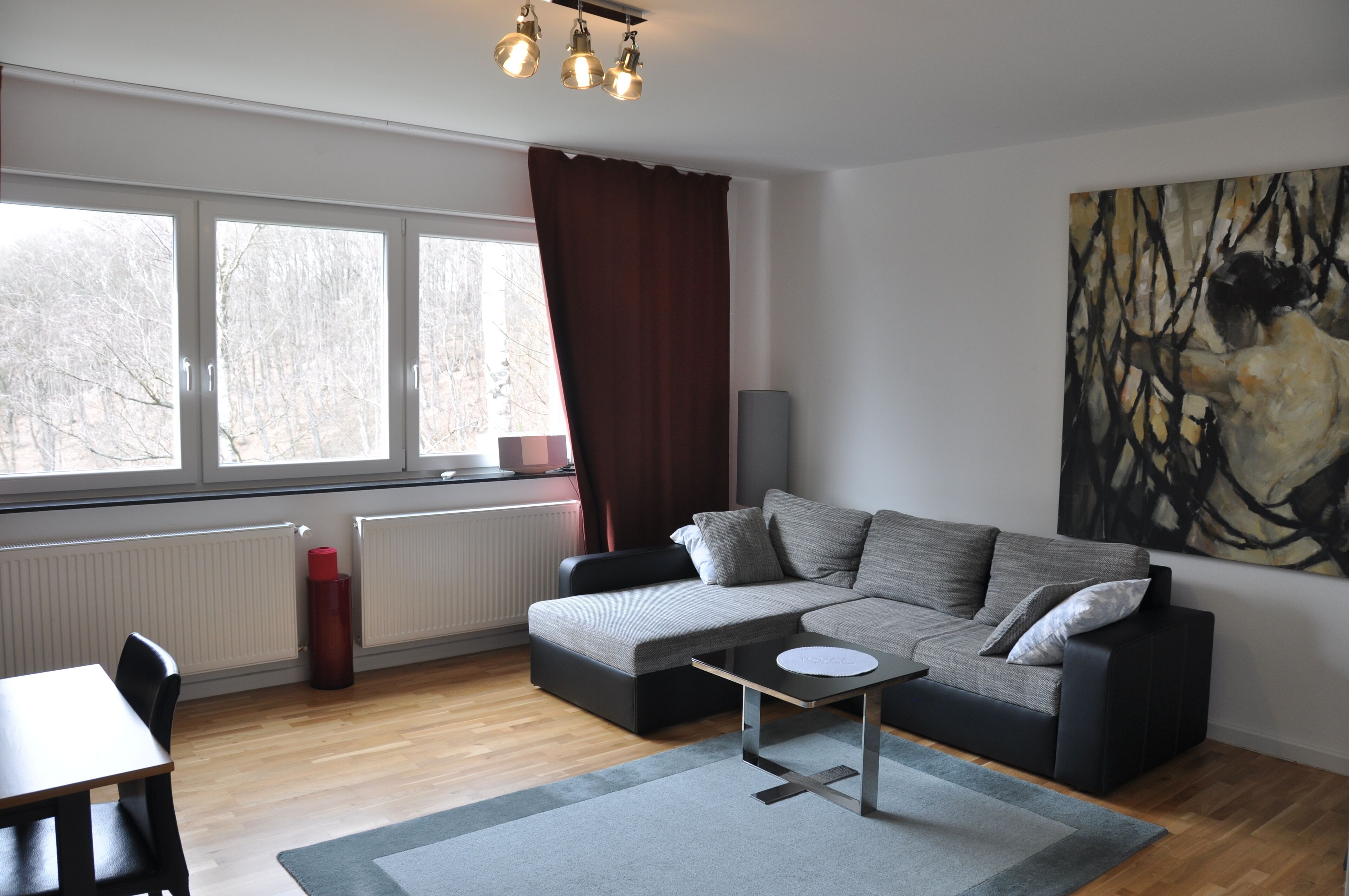 Ein modernes Wohnzimmer mit einem grauen Sofa, einem kleinen Tisch und einem großen abstrakten Gemälde an der Wand.