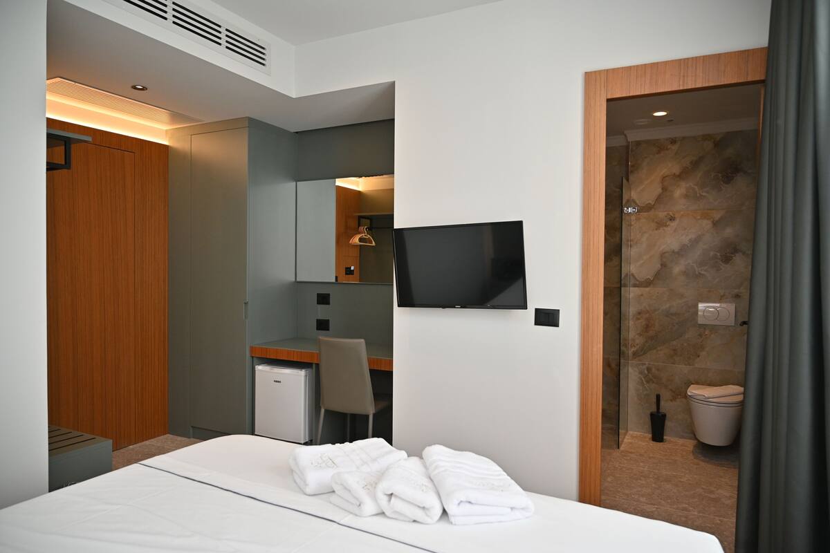 Ett modernt hotellrum med en säng, ett skrivbord, en tv och en duschhörna.